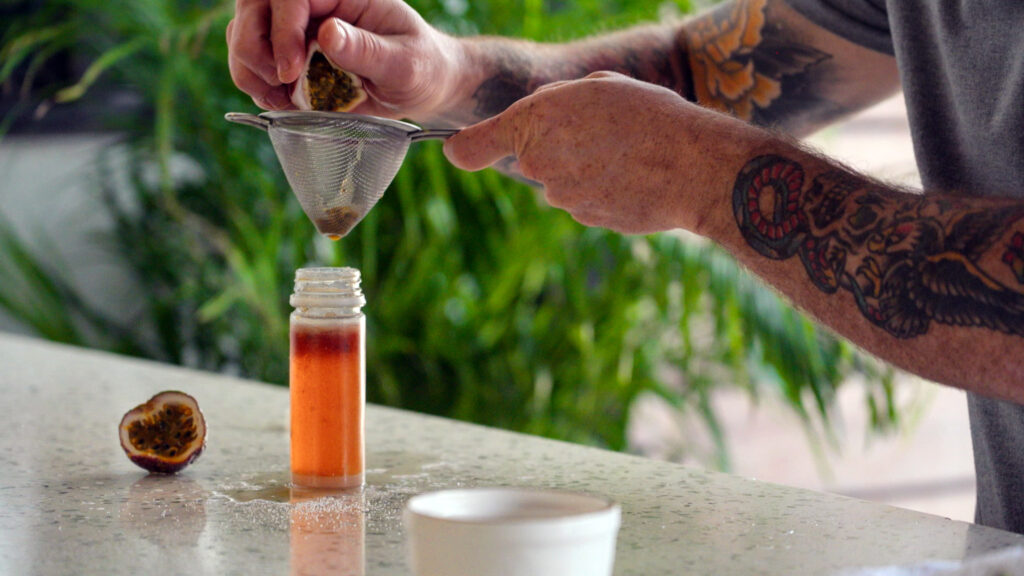 Close up of squeezing passion fruit juice into a sieve over bottle.